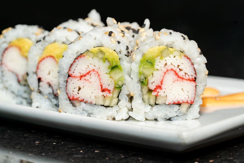  A zoomed in photo of a sushi roll on a white plate. Sushi roll consists of rice and seeds on the outside, krab, avocado, and cucumber. Go from sushi beginner to sushi expert after a delightful dining experience at Shogun Sakura Sushi on International Drive.