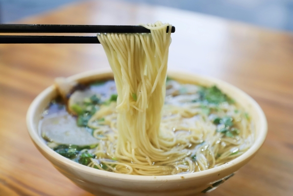 Chopsticks holding noodles over a bowl of ramen against a wooden tabletop. 