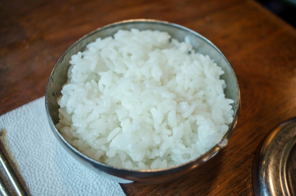 A bowl of white rice against a wooden background.