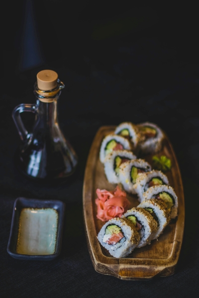 A wooden tray with ginger, wasabi, and a curving sushi roll beside a soy sauce dish and a glass bottle of soy sauce.  