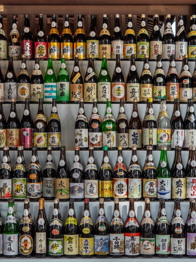 A large wall of sake bottles with colorful labels. 